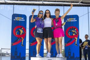 Radosne laureatki na podium z uniesionymi żółtymi nagrodami; po lewej numer 397, po prawej różowa spódnica i medal.