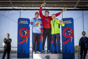 Trzej zawodnicy na stopniach podium trzymają żółte kartki z wynikami przed banerami zaBIEGaj o FUNdusze.