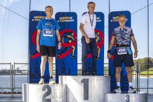 Trzech dojrzałych zawodników na podium z medalami; środkowy w białej koszulce, boczni w koszulkach biegu.