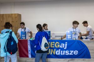 Wolontariusze w koszulkach Organizator przy ladzie odbioru numerów startowych w biurze zawodów biegu.