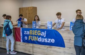 Szeroki widok biura zawodów z banerem zaBIEGaj o FUNdusze i stanowiskami numerów 200–499 za ladą.
