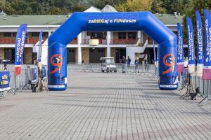 Niebieska brama dmuchana zaBIEGaj o FUNdusze nad kostką; flagi imprezy i budynek boiska w tle.