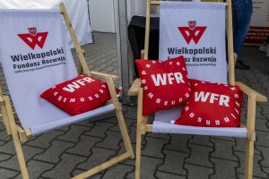 Dwa leżaki WFR z czerwonymi poduszkami z logotypem funduszu na kostce przed namiotem eventowym.