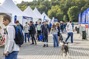 Tłum między białymi namiotami na Malcie; biegacz z medalem na szyi niesie niebieską torbę startową.