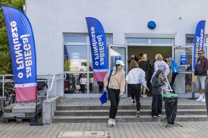 Wejście do biura zawodów ozdobione flagami zaBIEGaj o FUNdusze; ludzie wchodzą i schodzą po schodach.
