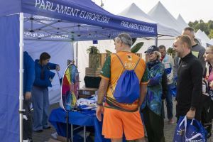Koło fortuny na stoisku Parlamentu Europejskiego; biegacz w koszulce Wałbrzych i obsługa w niebieskich bluzach.