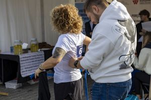 Mężczyzna przypina niebieski numer startowy na plecy biegaczki przy stole WFR z dyspenserami lemoniady.