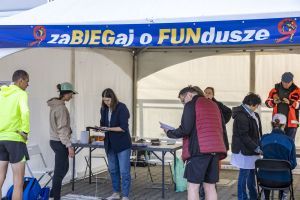 Rejestracja pod namiotem z banerem zaBIEGaj o FUNdusze; wolontariuszka z tabletem obsługuje kolejkę biegaczy.
