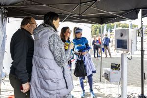Grupa przy mobilnej fotobudce z drukarką zdjęć pod czarnym namiotem na kostce w strefie biegaczek.