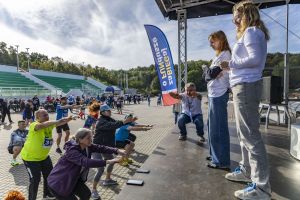 Rozgrzewka przysiadów przed startem: tłum na bruku naśladuje instruktora na podwyższonej scenie przy trybunach.
