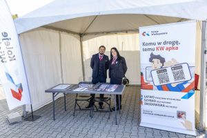Dwójka pracowników Kolei Wielkopolskich w mundurach przy stoisku z banerem aplikacji KW w namiocie.