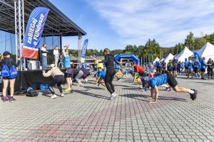 Tłum na placu wykonuje burpees pod okiem instruktorów na scenie z flagami zaBIEGaj o FUNdusze.