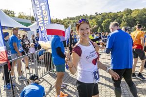 Uśmiechnięta biegaczka z numerem 17 trzyma flagi Polski i Unii Europejskiej w koszulce Fundacji Dzięki Tobie.